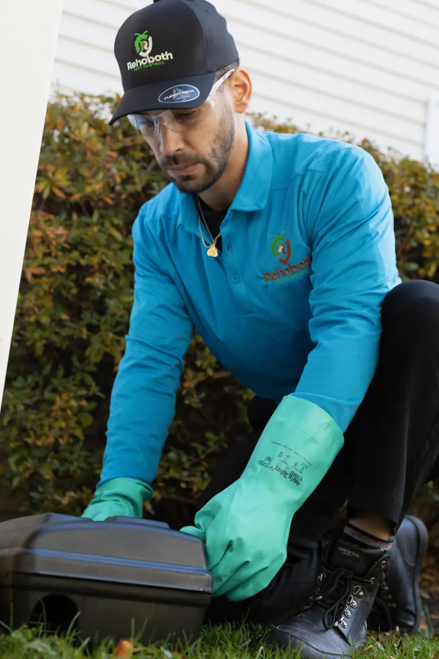 Technician placing a rodent bait station beside a home