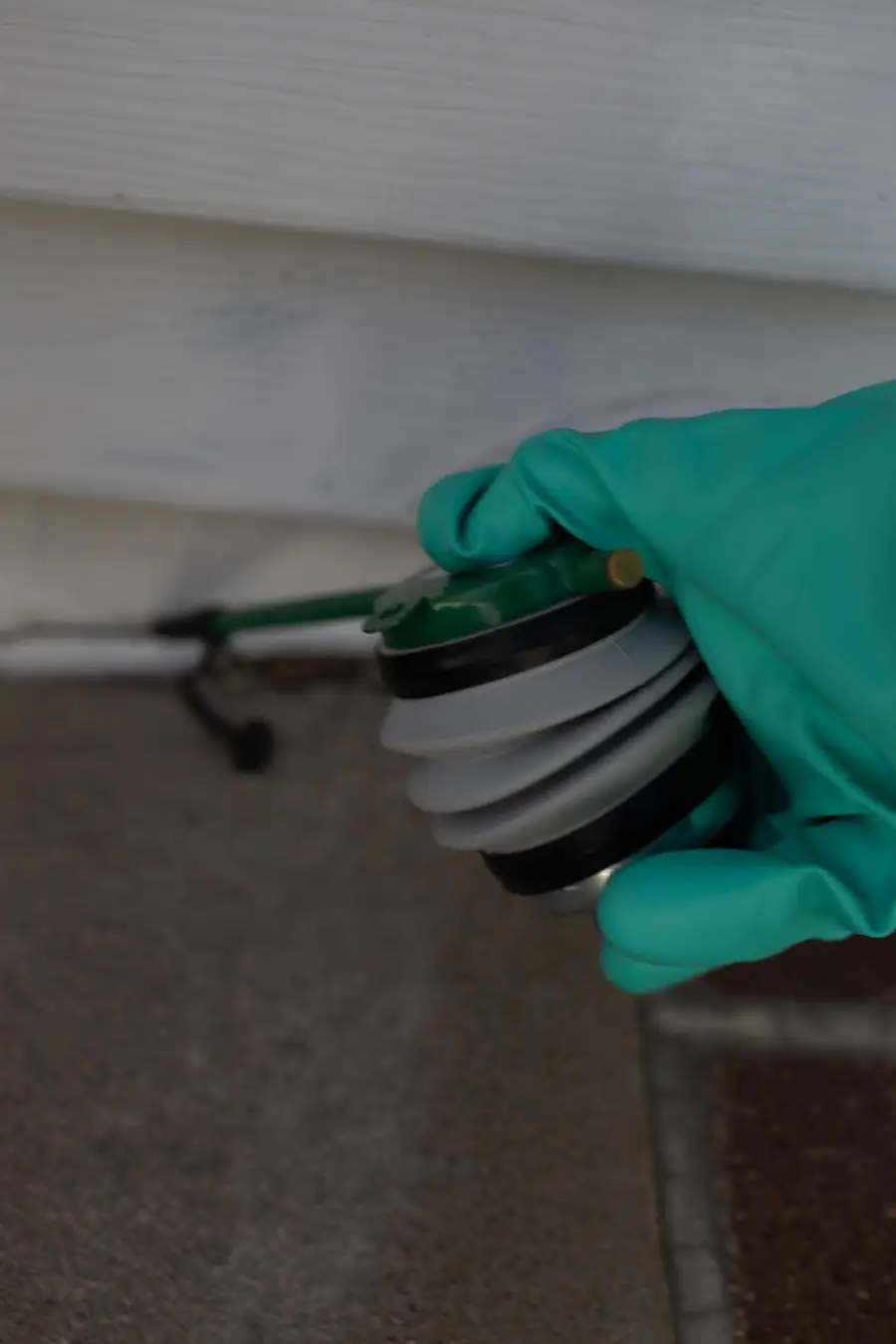 Gloved hand applying dust into a gap in a home's siding