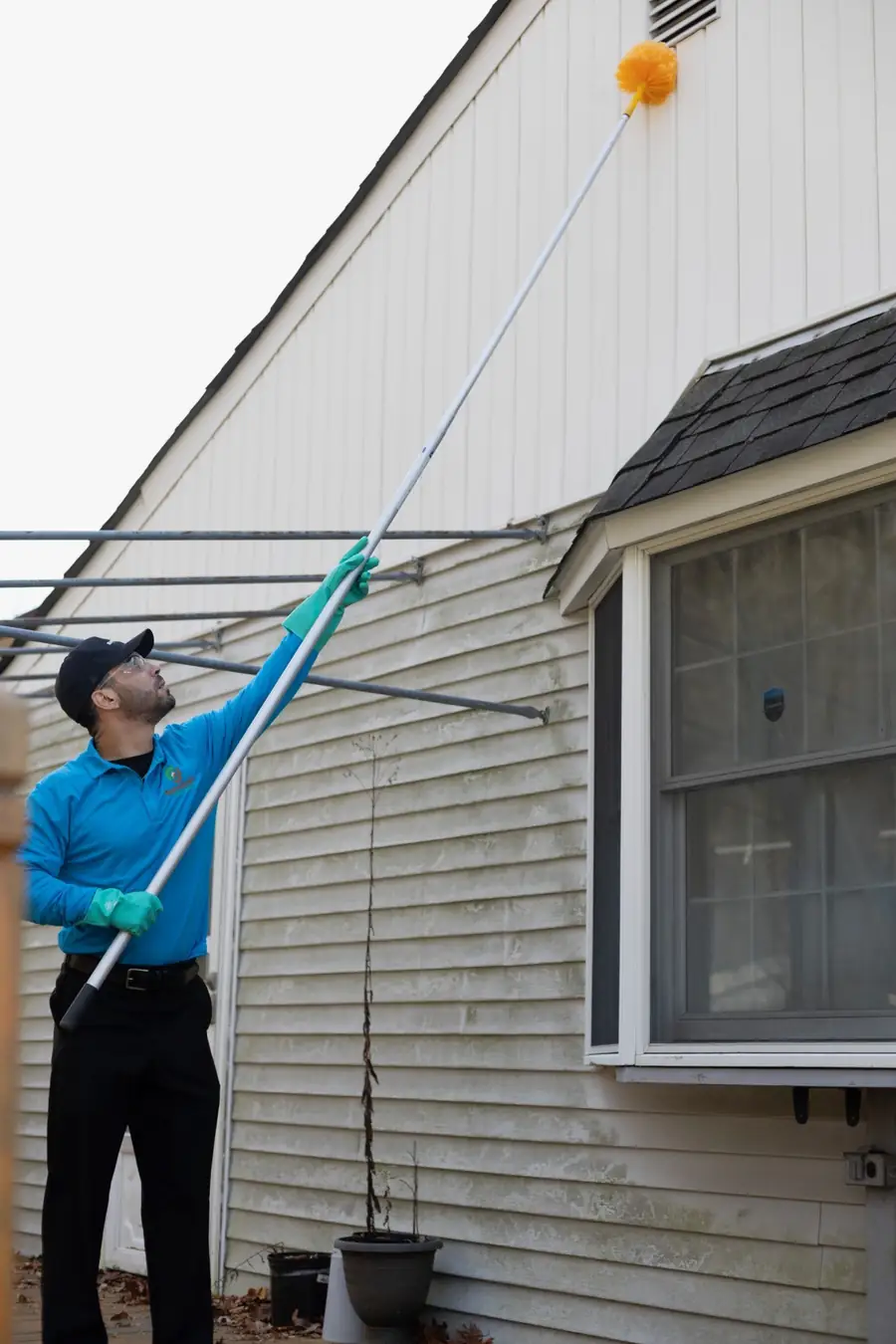 Technician sweeping webs from a gable vent with an extension duster