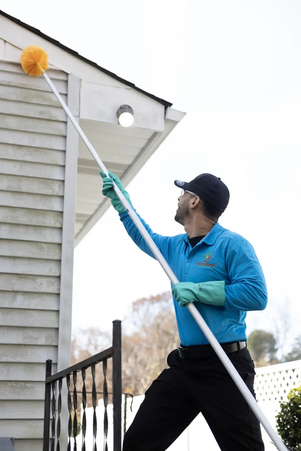 Technician sweeping webs and nests from the eaves with an extension duster
