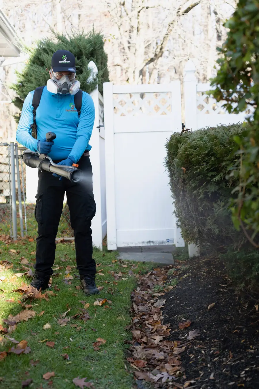 Technician in a respirator misting shrubs for mosquitoes and ticks