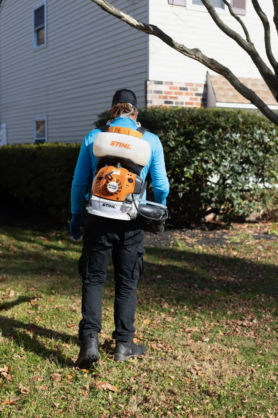 Technician carrying a backpack mister across a back yard