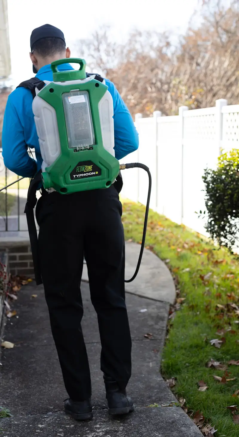 Technician with a backpack sprayer along a side walkway